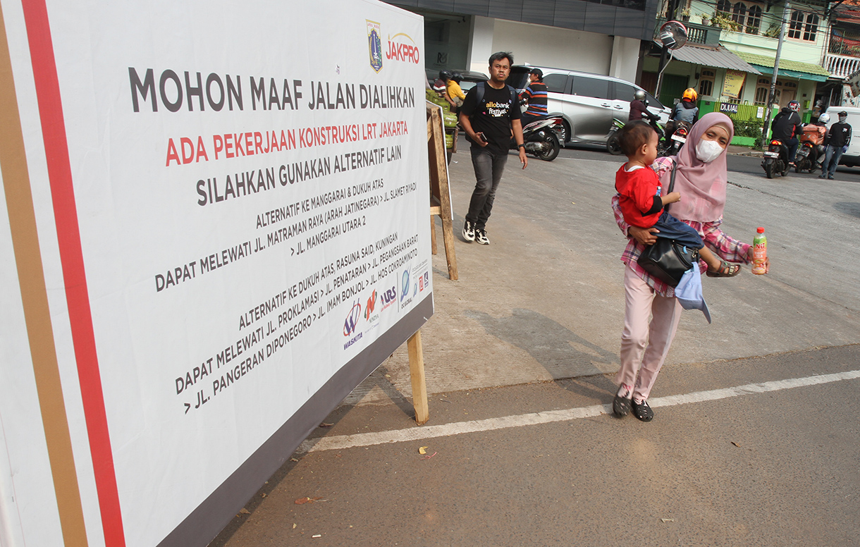 Warga melintas di depan papan informasi pengalihan arus lalu lintas akibat proyek pembangunan jalur kereta ringan atau Lintas Rel Terpadu (LRT) Jakarta Fase 1B rute Velodrome-Manggarai di Jalan Tambak, Jakarta, Minggu (15/9/2024).  (BeritaNasional.com/ Oke Atmaja)