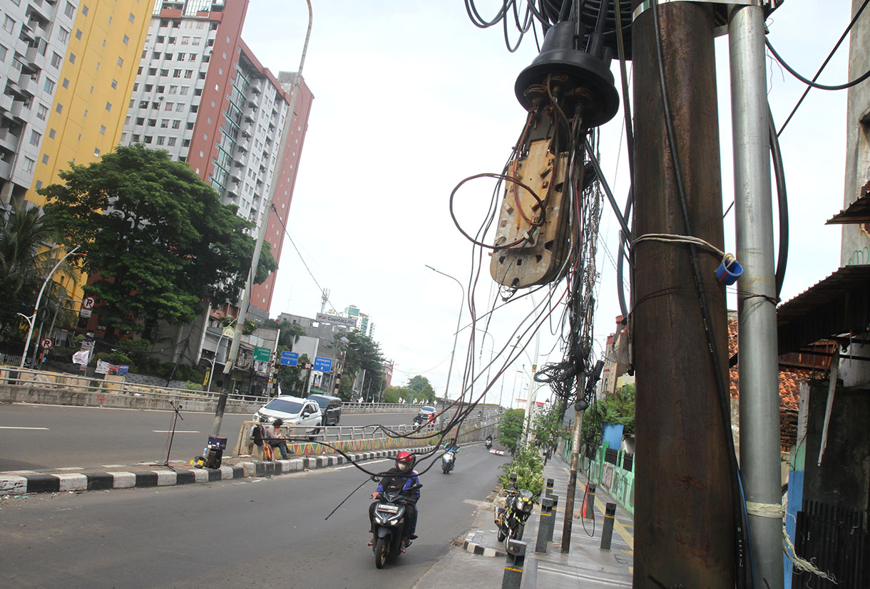 Sejumlah pengendara sepeda motor melintasi jalur pedestrian di bawah kabel yang semrawut di Jalan Matraman Raya, Jakarta, Senin (18/11/2024).  (BeritaNasional.com/Oke Atmaja)