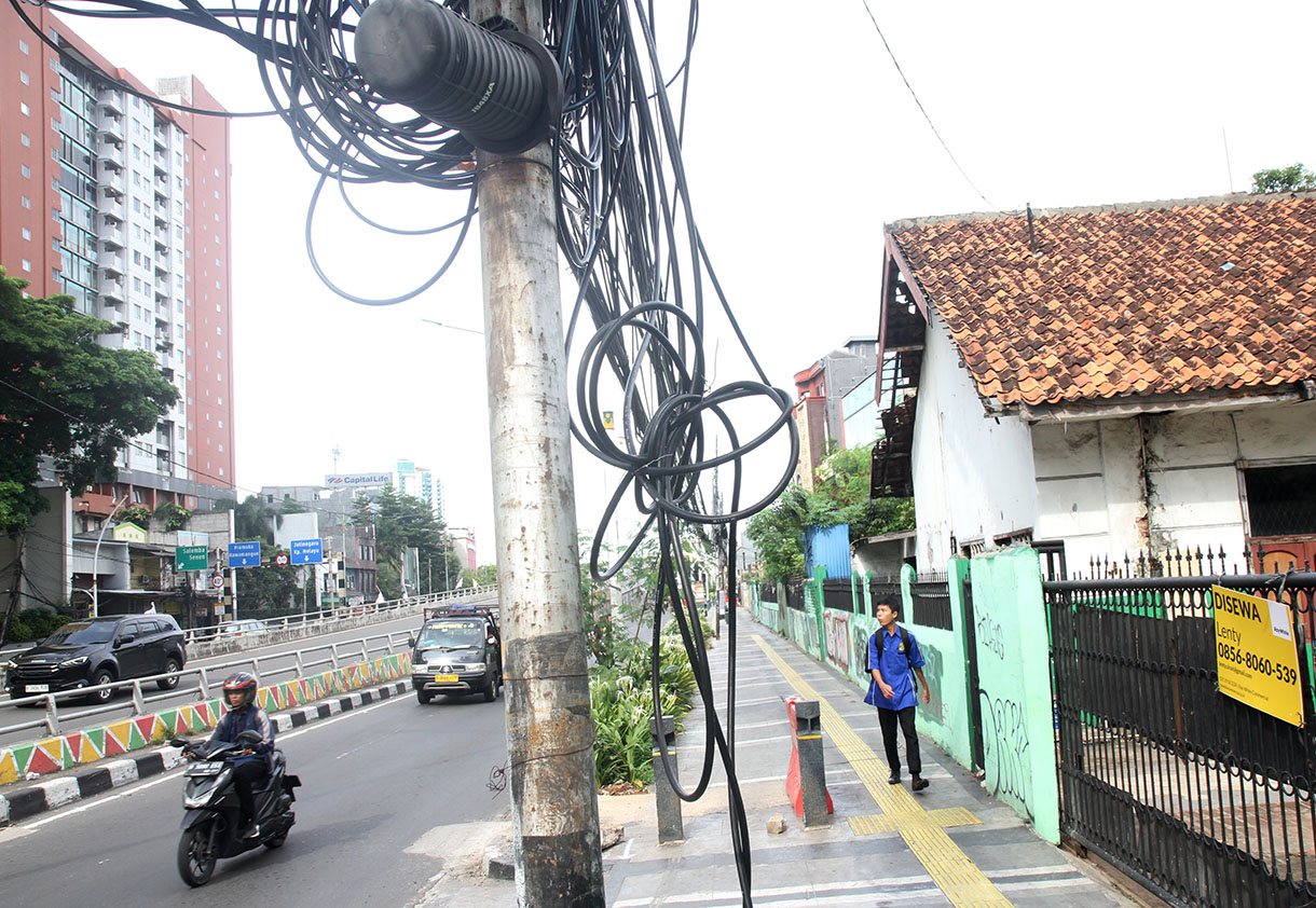 Sejumlah pengendara sepeda motor melintasi jalur pedestrian di bawah kabel yang semrawut di Jalan Matraman Raya, Jakarta, Senin (18/11/2024).  (BeritaNasional.com/Oke Atmaja)