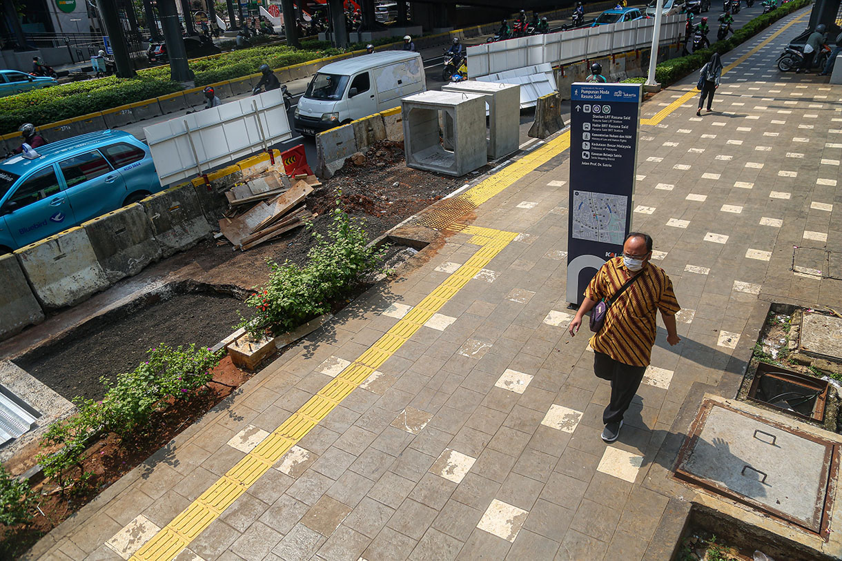 Pejalan kaki melintasi proyek revitalisasi trotoar di Jalan Rasuna Said, Kuningan, Jakarta, Selasa (8/10/2024).(BeritaNasional.com/Oke Atmaja)