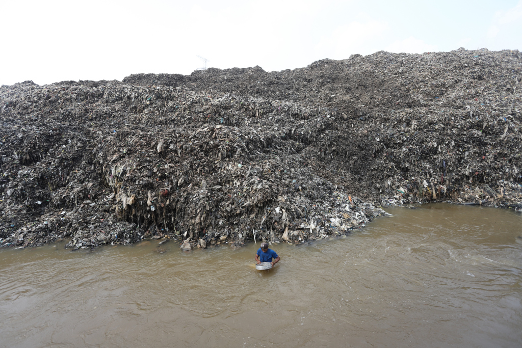 Pemulung menyeberangi Kali Pesanggrahan sambil membawa sampah untuk didaur ulang di Tempat Pembuangan Akhir Cipayung, Depok, Jawa Barat, Kamis (9/5/2024).  (BeritaNasional.com/Oke Atmaja)