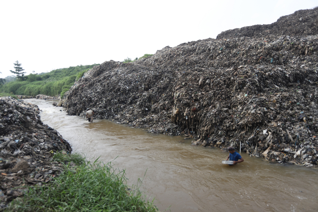 Pemulung menyeberangi Kali Pesanggrahan sambil membawa sampah untuk didaur ulang di Tempat Pembuangan Akhir Cipayung, Depok, Jawa Barat, Kamis (9/5/2024).  (BeritaNasional.com/Oke Atmaja)