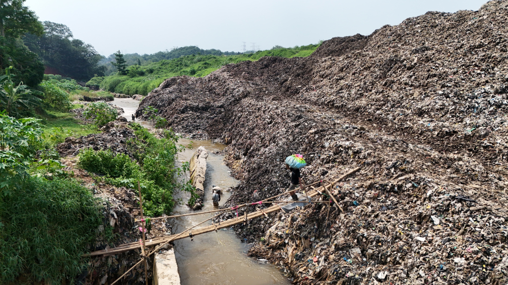 Pemulung menyeberangi Kali Pesanggrahan sambil membawa sampah untuk didaur ulang di Tempat Pembuangan Akhir Cipayung, Depok, Jawa Barat, Kamis (9/5/2024).  (BeritaNasional.com/Oke Atmaja)