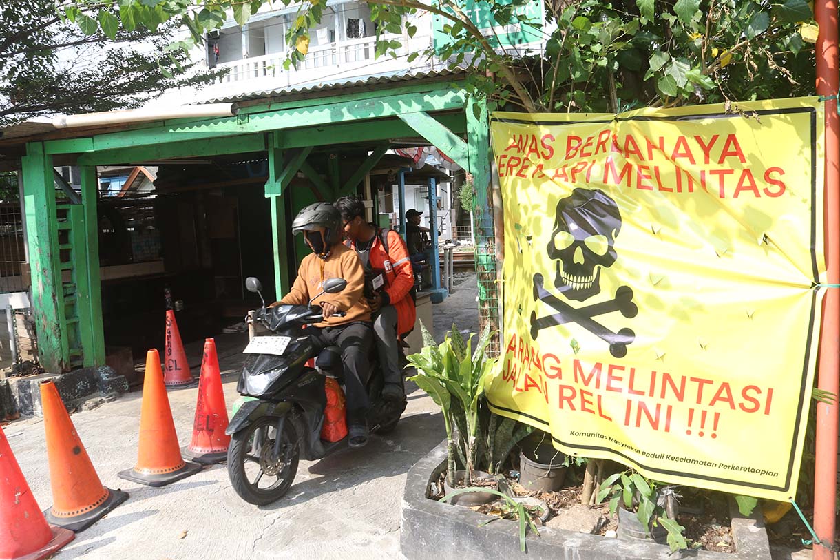 Pengendara melintas di samping spanduk peringatan dan larangan melintas di perlintasan liar jalur kereta api di kawasan Tebet, Jakarta, Selasa (19/5/2026).  (Beritanasional.com/Oke Atmaja)