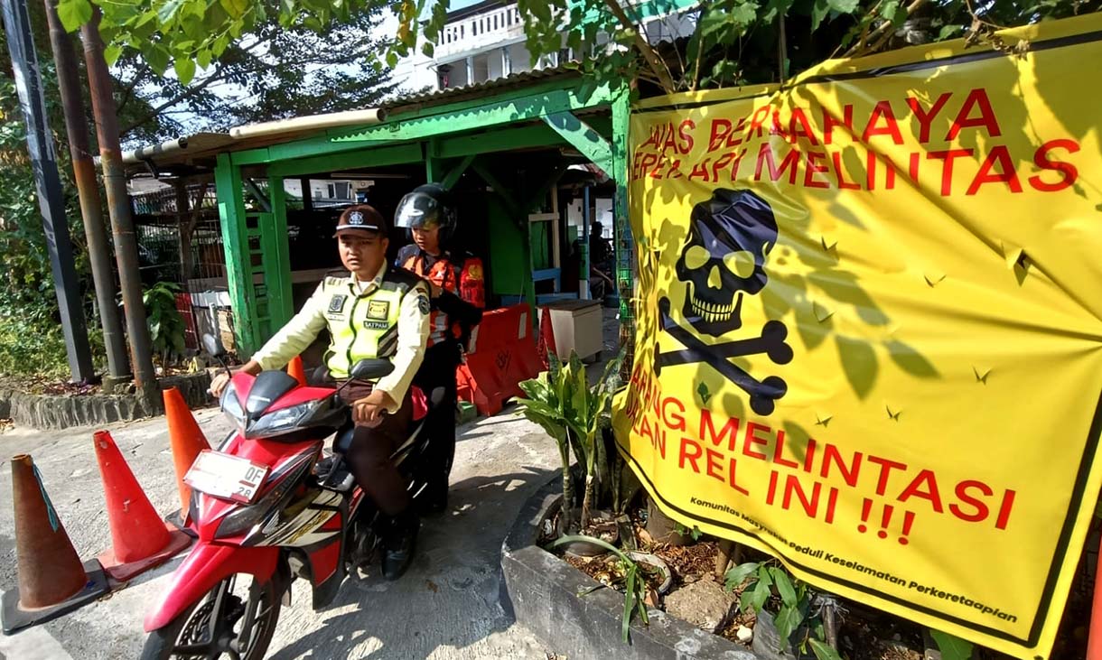Pengendara melintas di samping spanduk peringatan dan larangan melintas di perlintasan liar jalur kereta api di kawasan Tebet, Jakarta, Selasa (19/5/2026).  (Beritanasional.com/Oke Atmaja)
