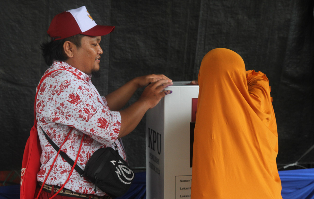 Petugas Kelompok Penyelenggara Pemungutan Suara (KPPS) mengenakan seragam sekolah mengarahkan warga memasukkan surat suara di TPS 05 Petamburan, Tanah Abang, Jakarta, Rabu (27/11/2024).(BeritaNasional.com/Oke Atmaja)